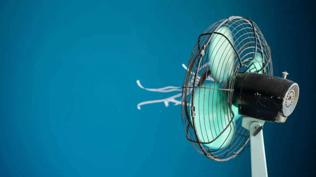An old electric fan with spinning blades and fluttering paper strips against a blue background.
