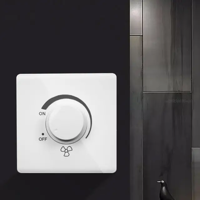 A close-up of a white, square ceiling fan speed switch mounted on a dark wall. The switch features a large, central rotary dial. An arc graphic indicates the "ON" position at the top and the "OFF" position at the bottom, with a fan icon printed below. This wall control allows for variable adjustment of the fan's speed.