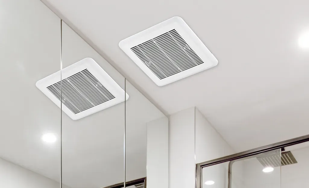 Ceiling-mounted dual bathroom exhaust fan grilles reflected in mirror