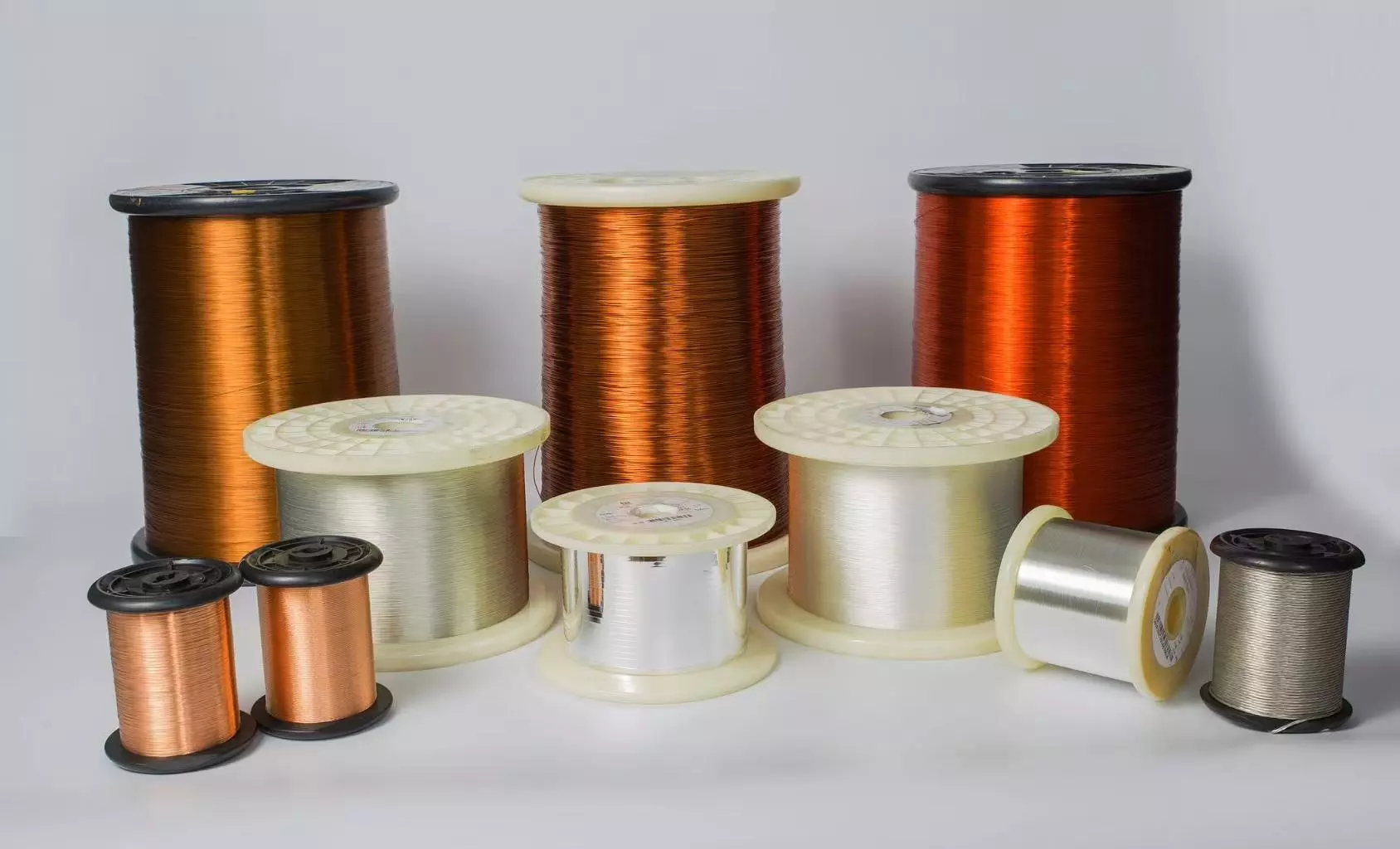 A collection of various spools containing reddish-brown copper wire and silver-colored aluminum wire arranged on a white background.